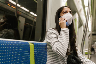 Woman looking away while talking on smart phone in metro train - EGAF00995