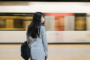 Woman waiting for her train at metro station during pandemic - EGAF00997