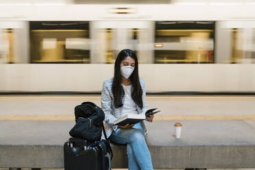 Woman reading book while sitting against moving train at metro station - EGAF00999