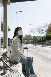 Frau wartet an einem sonnigen Tag während der COVID-19-Pandemie auf den Bus - EGAF01007