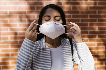 Woman wearing face mask against brick wall - EGAF01010