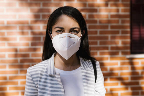 Selbstbewusste Frau mit Gesichtsschutzmaske vor einer Ziegelmauer während COVID-19 - EGAF01011