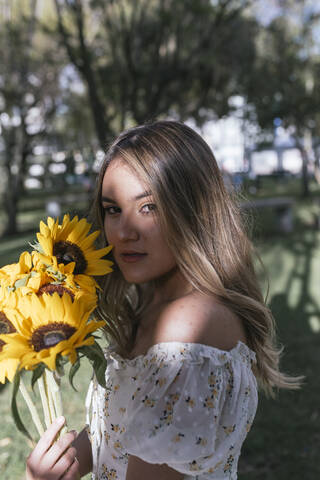 Frau hält Sonnenblumen, während sie im Hinterhof steht, lizenzfreies Stockfoto