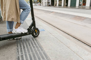 Woman standing with electric push scooter at tram station in city - VABF03975