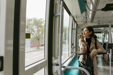 Frau mit Elektroroller schaut weg, während sie in der Straßenbahn mit dem Handy telefoniert - VABF03985