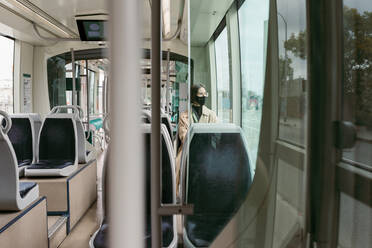 Frau mit Gesichtsmaske reist in der Straßenbahn sitzend - VABF03986