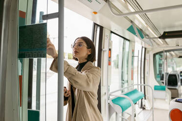Frau mit Mobiltelefon benutzt Fahrkartenautomat in der Straßenbahn - VABF03989