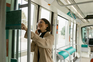 Lächelnde Frau, die in der Straßenbahn mit ihrem Handy telefoniert - VABF03990