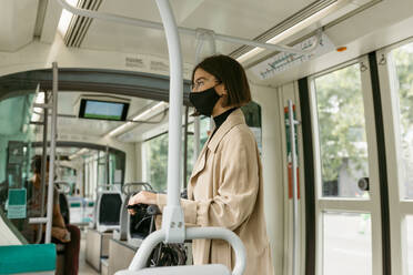 Mittlere erwachsene Frau mit Gesichtsmaske, die wegschaut, während sie mit einem Elektroroller in der Straßenbahn unterwegs ist - VABF03994
