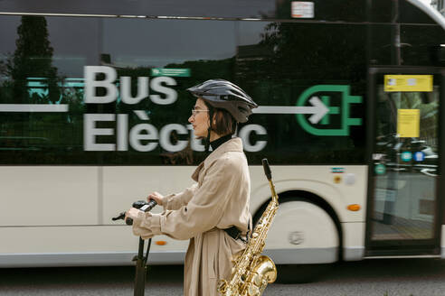 Frau mit Saxophon auf elektrischem Motorroller in der Stadt - VABF04011