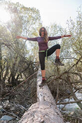 Mid adult woman standing with arms outstretched on fallen tree in forest at La Pedriza, Madrid, Spain - MRRF00645