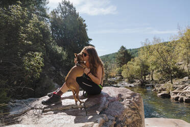 Woman kissing dog while sitting on rock in forest at La Pedriza, Madrid, Spain - MRRF00650