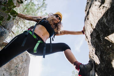 Frau mit Brille klettert auf einen Felsen gegen den klaren Himmel im Wald von La Pedriza, Madrid, Spanien - MRRF00658