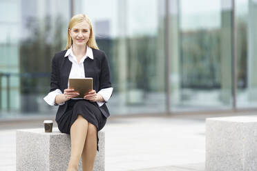 Smiling businesswoman using digital tablet while sitting on bench against building - GGGF00082