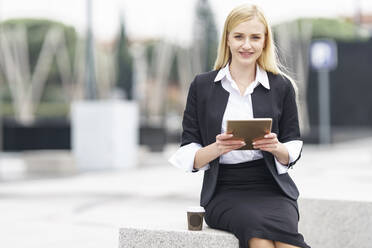 Young businesswoman using digital tablet while sitting on bench against building - GGGF00084