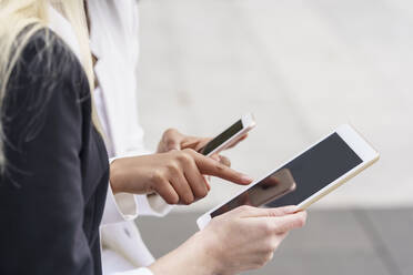 Geschäftsfrau, die auf ein digitales Tablet zeigt, während sie das Mobiltelefon eines Kollegen in der Stadt benutzt - GGGF00085