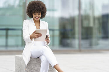 Businesswoman smiling while using digital tablet against building - GGGF00086