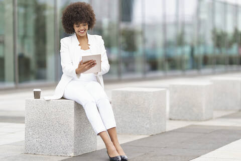 Businesswoman smiling while using digital tablet sitting on bench stock photo