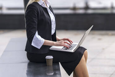 Businesswoman working on laptop while sitting on bench outdoors - GGGF00104