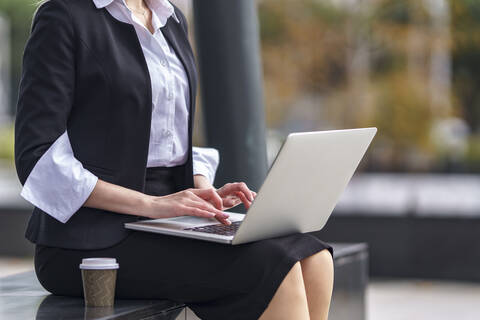 Businesswoman using laptop while sitting on bench outdoors stock photo