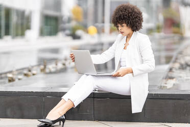 Businesswoman using laptop while sitting on bench outdoors - GGGF00106