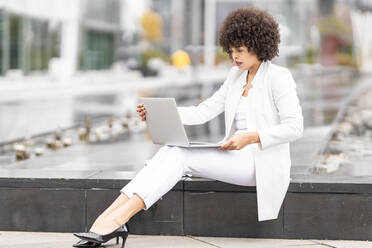Geschäftsfrau, die einen Laptop benutzt und auf einer Bank im Freien sitzt - GGGF00106