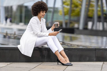 Geschäftsfrau trinkt Kaffee, während sie im Freien ein Mobiltelefon benutzt - GGGF00117