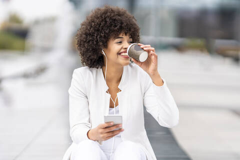 Smiling businesswoman with mobile phone drinking coffee while sitting at city stock photo