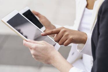 Geschäftsfrau, die auf ein digitales Tablet zeigt, während ein Kollege ein Mobiltelefon hält - GGGF00123