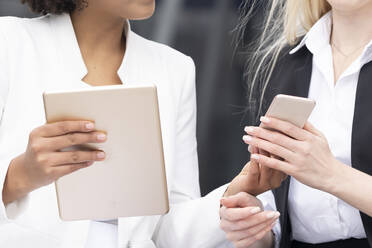 Geschäftsfrauen tauschen Mobiltelefon und digitales Tablet mit einem Kollegen im Freien aus - GGGF00124