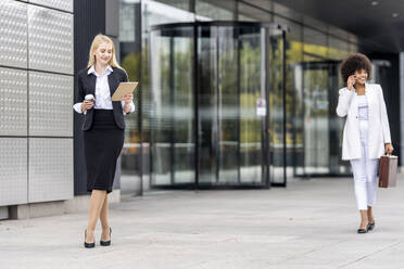 Businesswoman using digital tablet while standing with colleague in background against building - GGGF00128