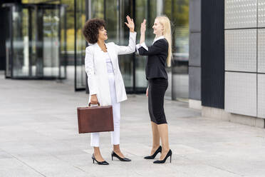 Businesswomen giving high five while standing on footpath - GGGF00130