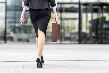 Businesswoman wearing high heels walking with briefcase on footpath - GGGF00133