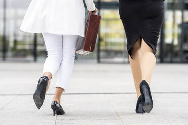 Businesswomen wearing high heels walking on footpath - GGGF00139