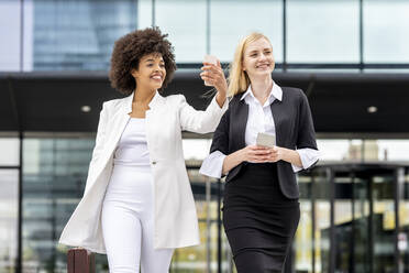 Young businesswoman using mobile phone while walking with colleague against building - GGGF00140