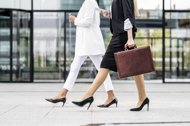 Businesswoman with briefcase using mobile phone while walking by colleague on footpath - GGGF00142