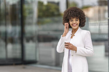 Lächelnde Geschäftsfrau, die im Freien stehend mit ihrem Mobiltelefon spricht - GGGF00151