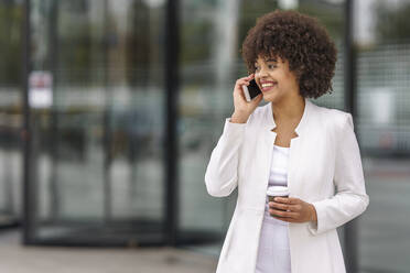 Businesswoman with coffee cup talking on mobile phone while standing outdoors - GGGF00153