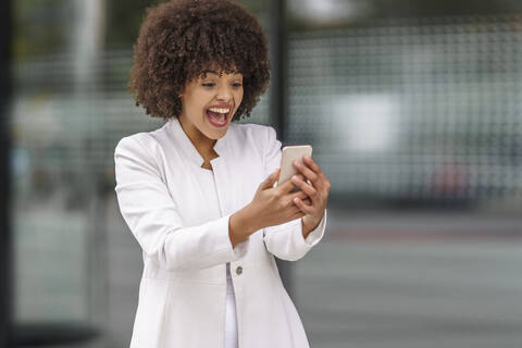 Glückliche Geschäftsfrau, die im Freien stehend auf ihr Mobiltelefon schaut, lizenzfreies Stockfoto