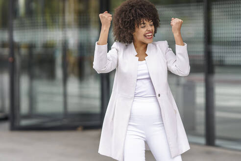 Smiling businesswoman showing winning gesture while standing outdoors - GGGF00159