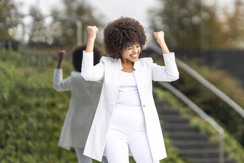 Young businesswoman showing winning gesture while standing against glass wall at city - GGGF00168