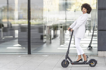 Excited businesswoman riding electric push scooter against building - GGGF00177