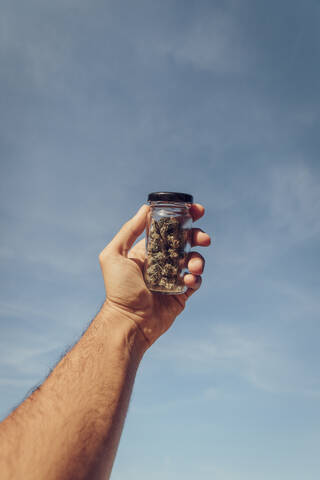 Man holding small marijuana jar against sky stock photo