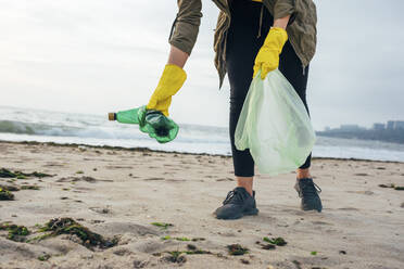 Umweltschützer mit Müllsack, der den Strand säubert, während er gegen den klaren Himmel steht - OYF00245