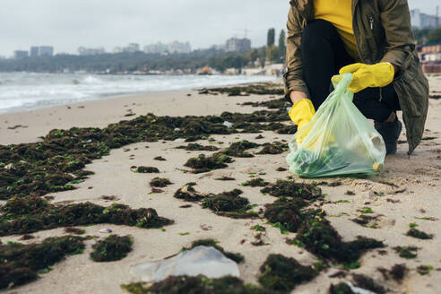Umweltschützer, der am Strand hockend Müll in einem Müllsack sammelt - OYF00247