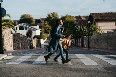 Woman and girl running while crossing road at city - EBBF01416