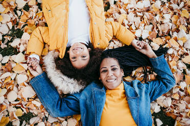 Smiling mother and daughter lying on fallen leaves at park - EBBF01422