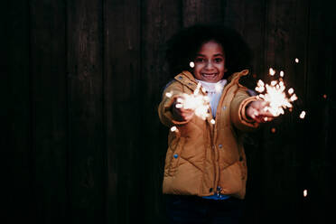 Smiling girl standing and playing with sparkler at night - EBBF01446