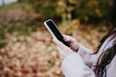 Hand einer Frau, die ein Smartphone benutzt, während sie im Herbst im Freien steht - EBBF01459
