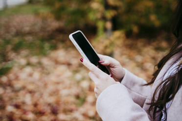 Hand of woman using smart phone while standing outdoors during autumn - EBBF01459